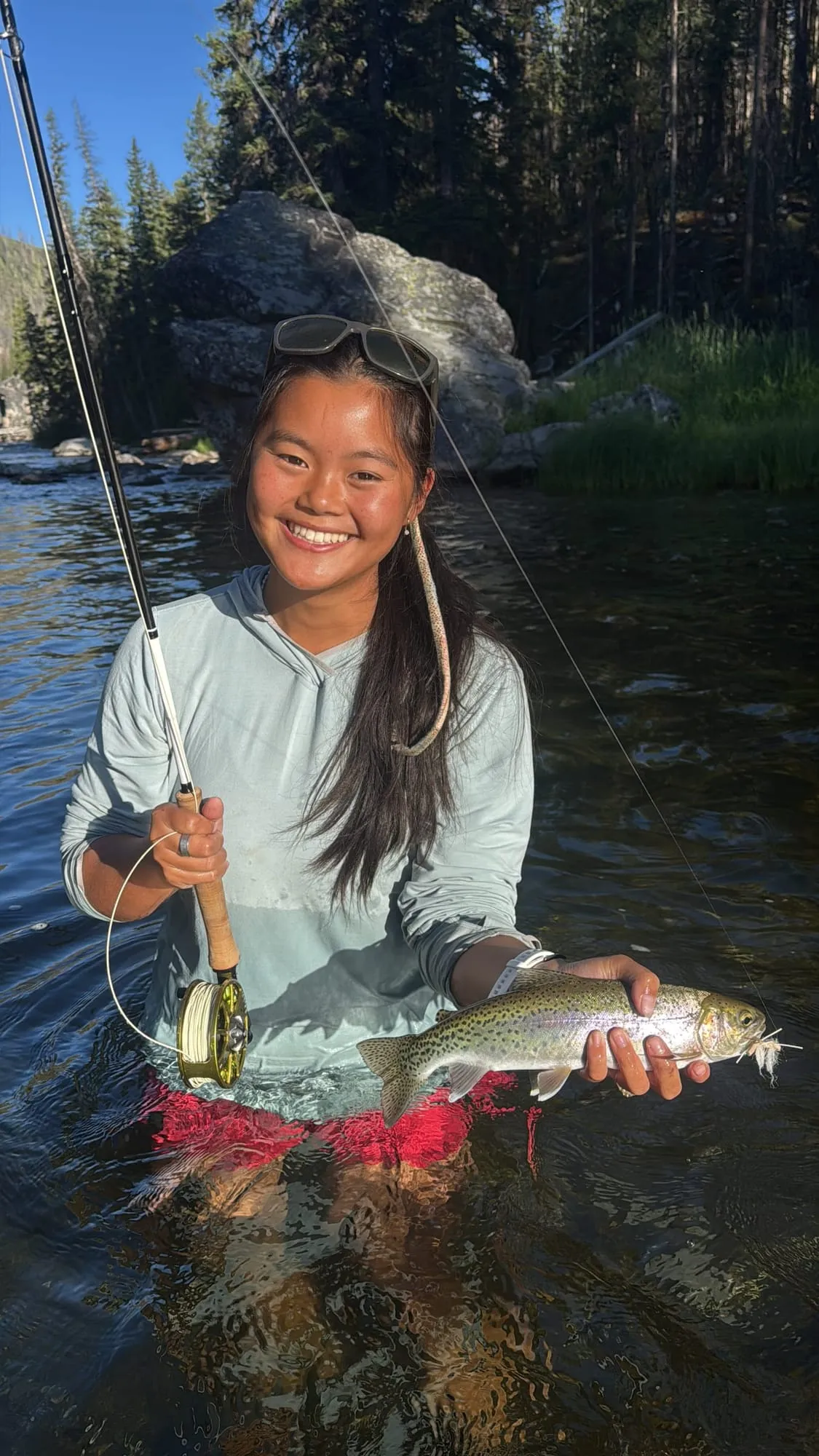 A trout held up while wading a mountain stream