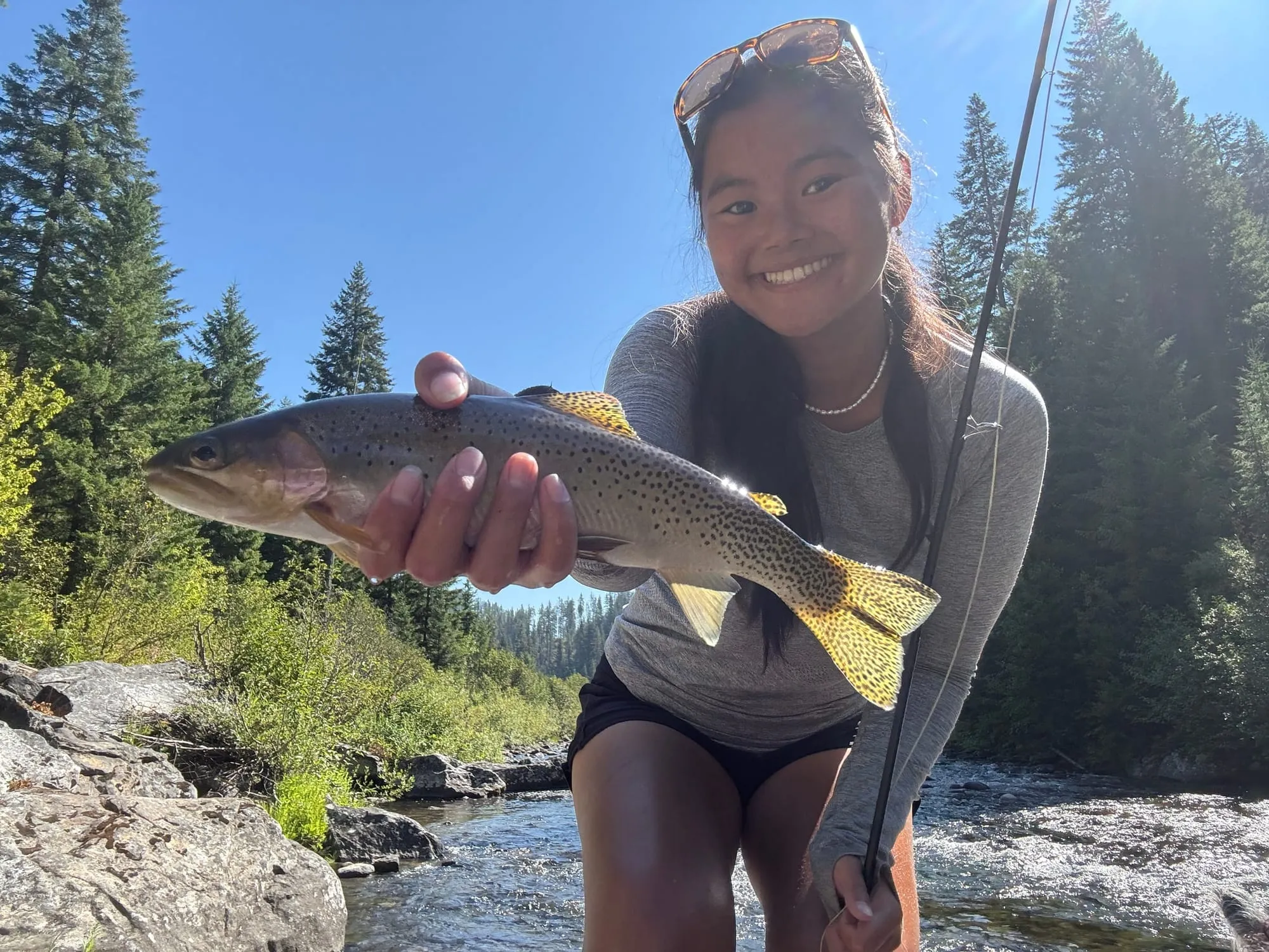 A cutthroat held up beside the rapids