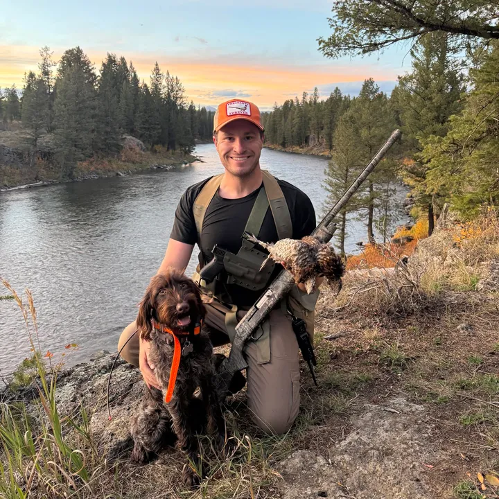 Fisher kneeling with Odin along the river after a hunt